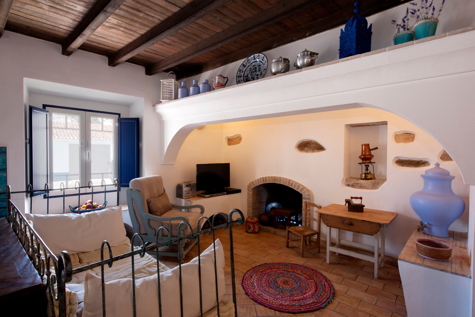 Sala de estar com lareira em tijolo, vigas de madeira à vista e cerâmica antiga