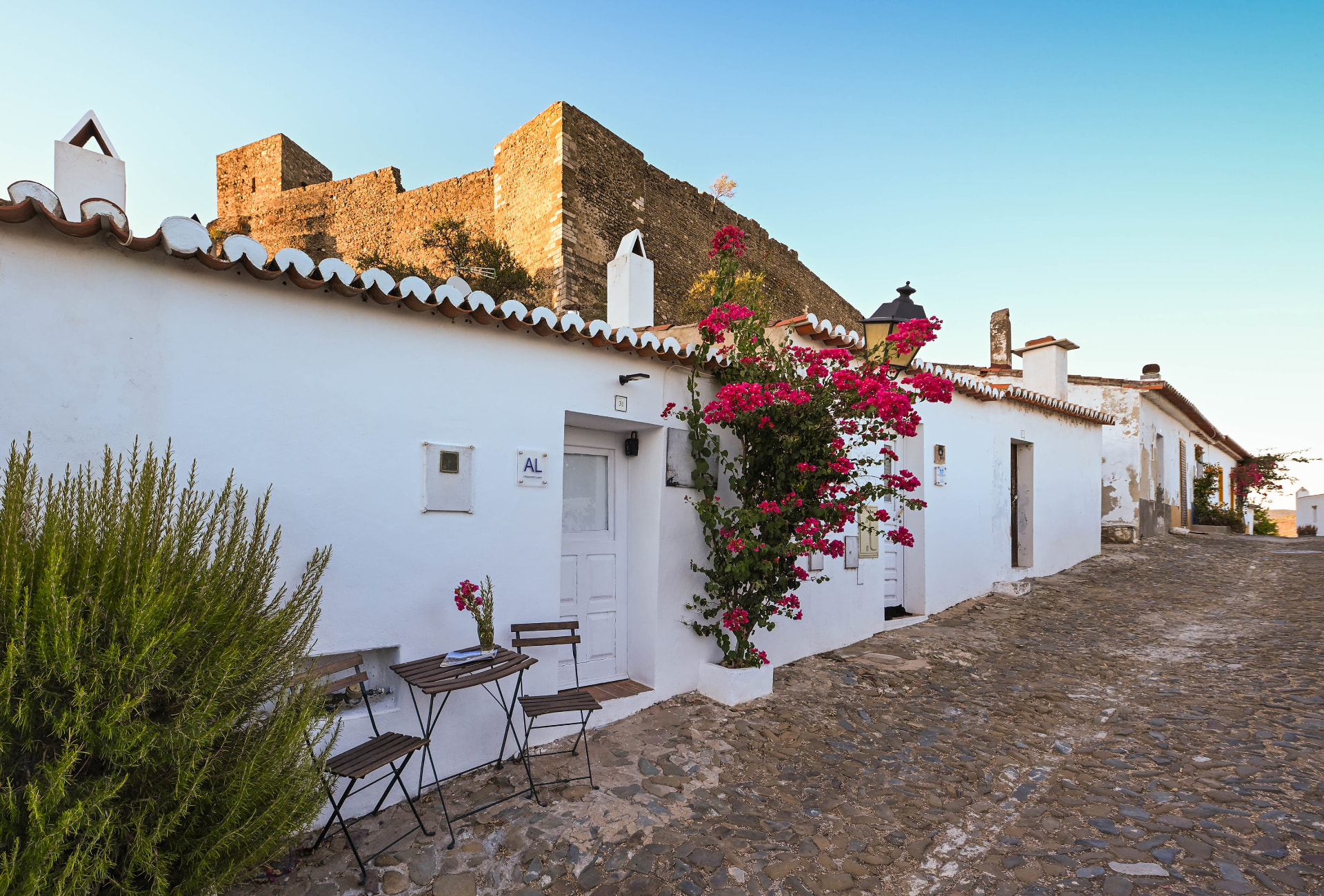 Fachada branca da Casa do Castelo com buganvílias e o castelo de Mértola ao fundo